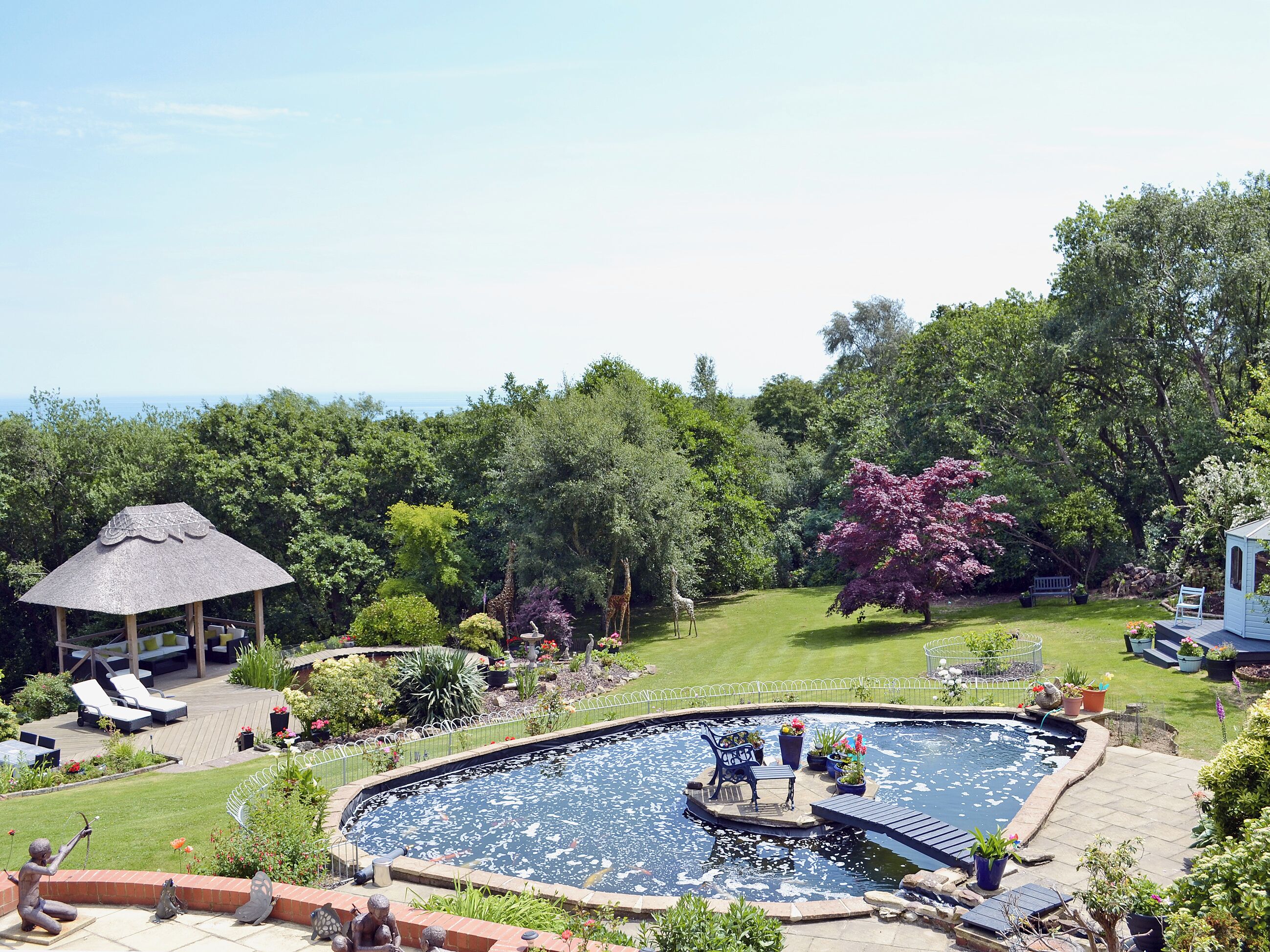 A backyard with a swimming pool, lounge chairs, a gazebo, and a variety of plants.
