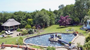 A backyard with a swimming pool, lounge chairs, a gazebo, and a variety of plants.