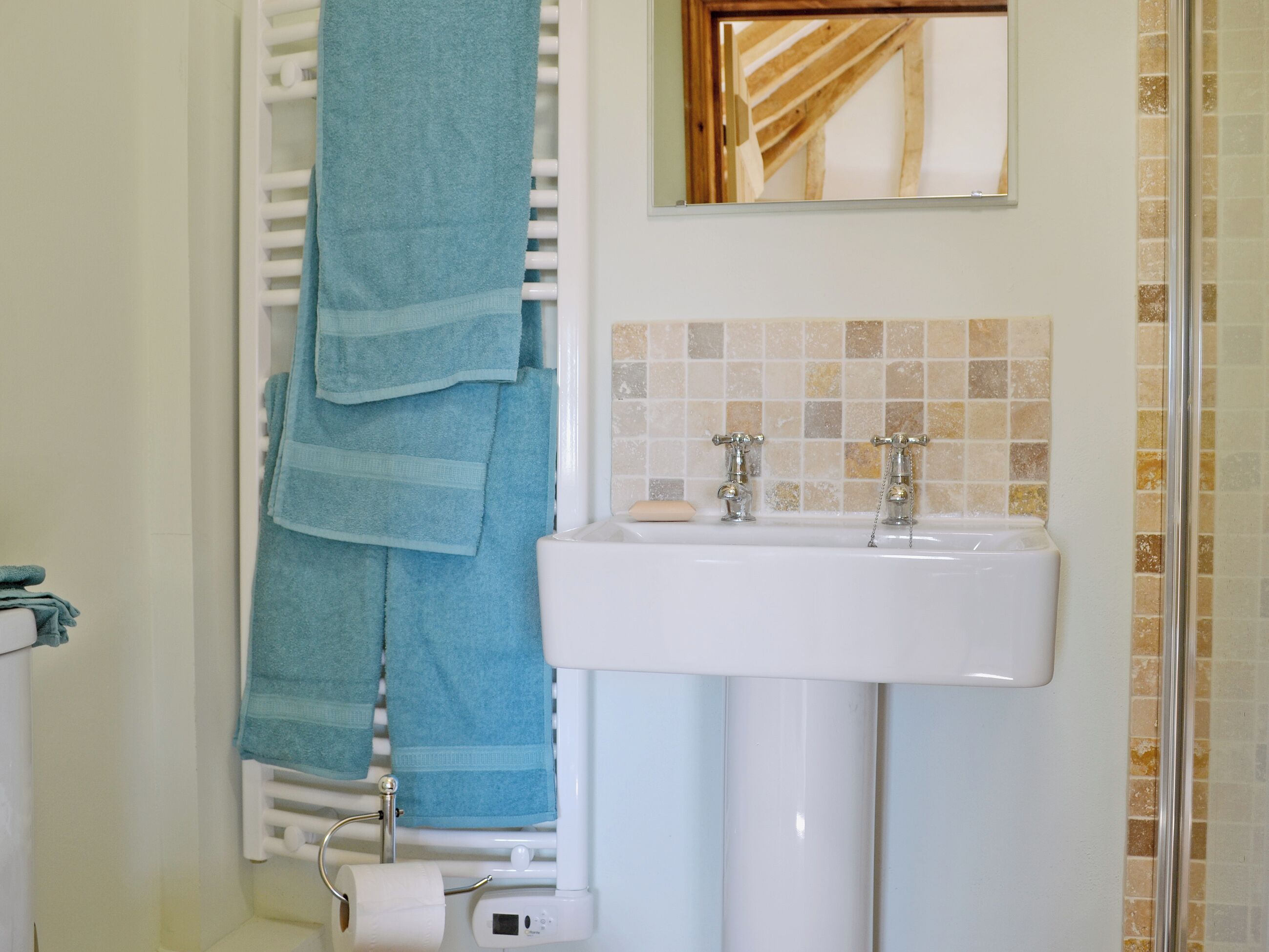 Ein Badezimmer mit einem weißen Waschbecken, zwei Wasserhähnen, einem Handtuchhalter mit blauen Handtüchern, einem Toilettenpapierhalter und einem Spiegel über dem Waschbecken.