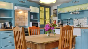 A kitchen with blue cabinets, a wooden dining table, and chairs. There is a vase with flowers on the table. - 2 bedroom accommodation in Trewalder, near Wadebridge (Trewalder, near Wadebridge)