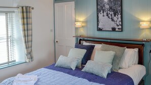 A bedroom with a bed, pillows, a headboard, a window with curtains, a door, and a wall-mounted picture. - 2 bedroom accommodation in Trewalder, near Wadebridge (Trewalder, near Wadebridge)