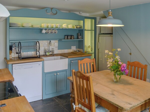 Een keuken met een spoelbak, vaatwasser en houten stoelen rond een tafel met een bloevas.