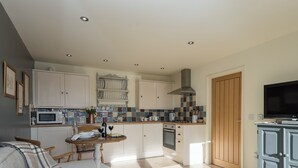 A modern kitchen with white cabinets, a microwave, and a gas stove. There is a dining area with a table and chairs, and a TV mounted on a cabinet. - 1 bedroom accommodation in South Elkington, near Louth (South Elkington, near Louth)