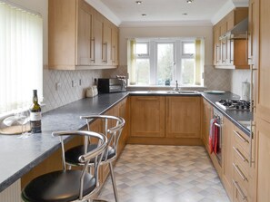 A modern kitchen with wooden cabinets, a black countertop, a built-in stove, and a window with curtains.