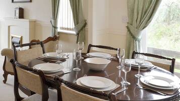 A dining table set for six with six chairs, a clock on the wall, and a window with curtains.