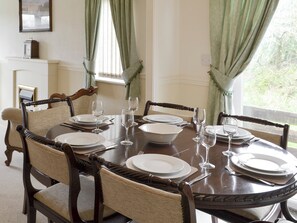 A dining table set for six with six chairs, a clock on the wall, and a window with curtains. - 2 bedroom accommodation in Woodacott, near Holsworthy (Woodacott, near Holsworthy)