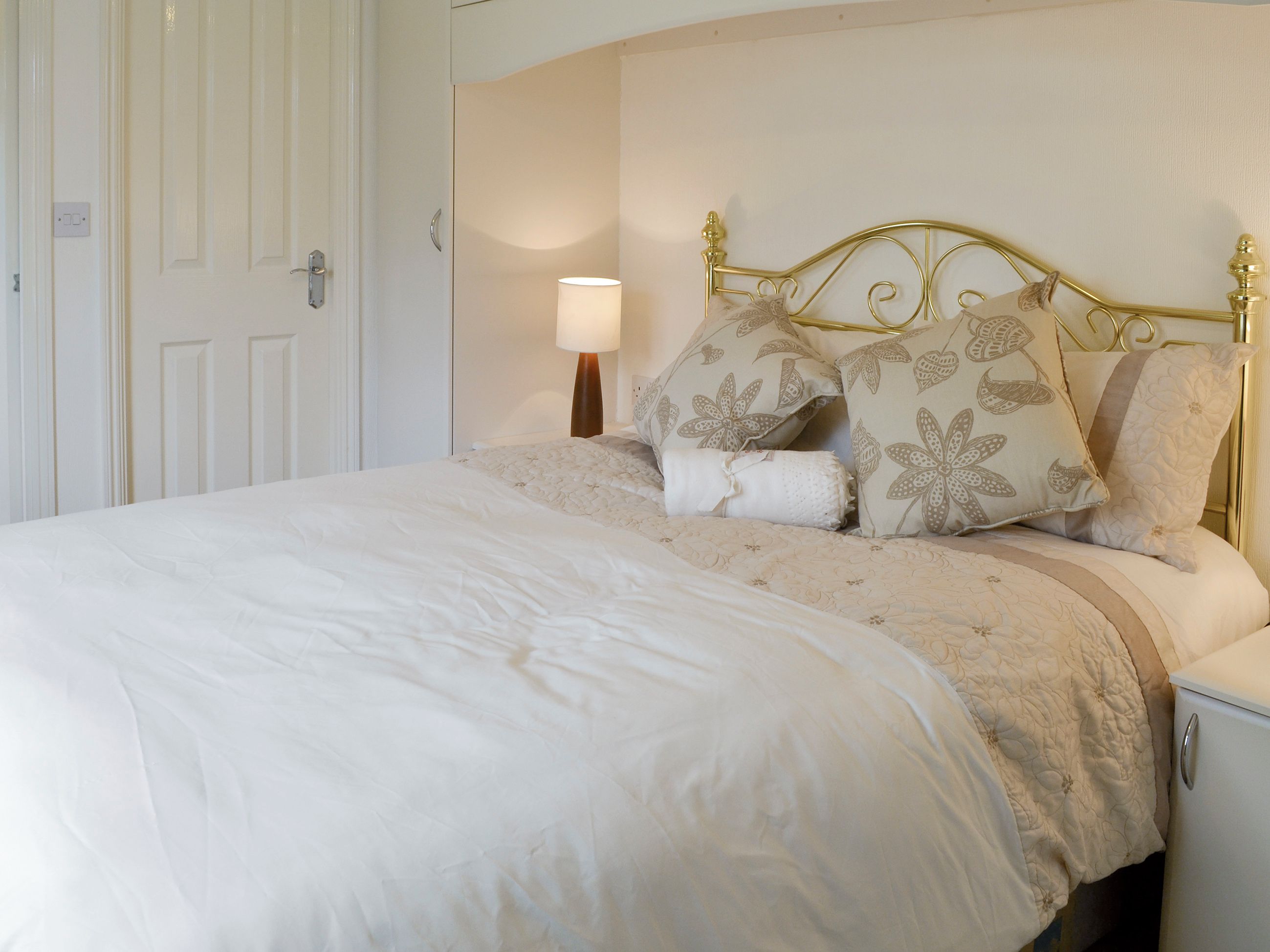 A neatly made bed with a floral-patterned headboard and pillows, a bedside lamp, and a white nightstand.
