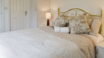 A neatly made bed with a floral-patterned headboard and pillows, a bedside lamp, and a white nightstand.