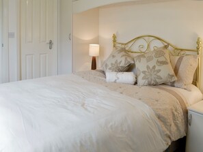 A neatly made bed with a floral-patterned headboard and pillows, a bedside lamp, and a white nightstand.