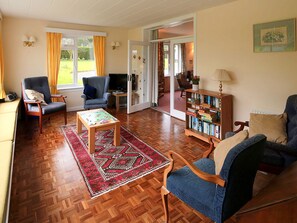 Un salon chaleureux avec un plancher en bois, une table basse, deux fauteuils, une bibliothèque et un téléviseur.