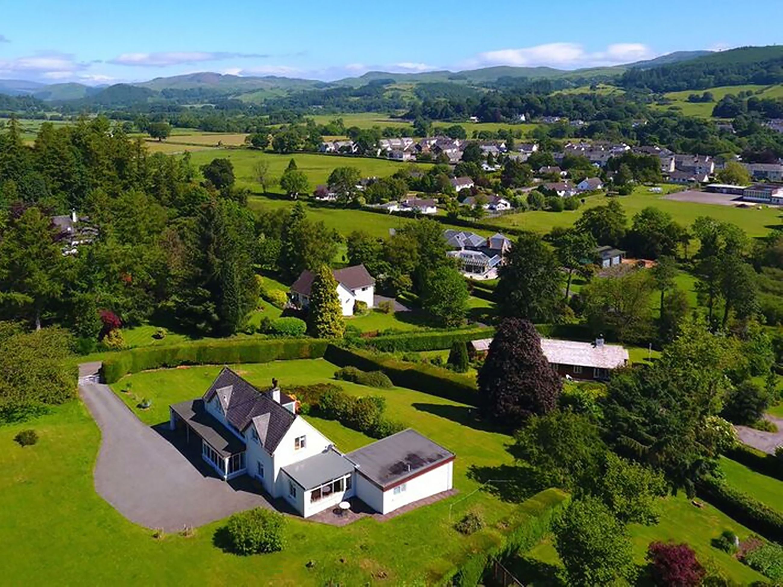 An aerial view of a residential area with houses, green fields, and a large estate with a driveway and a white building.