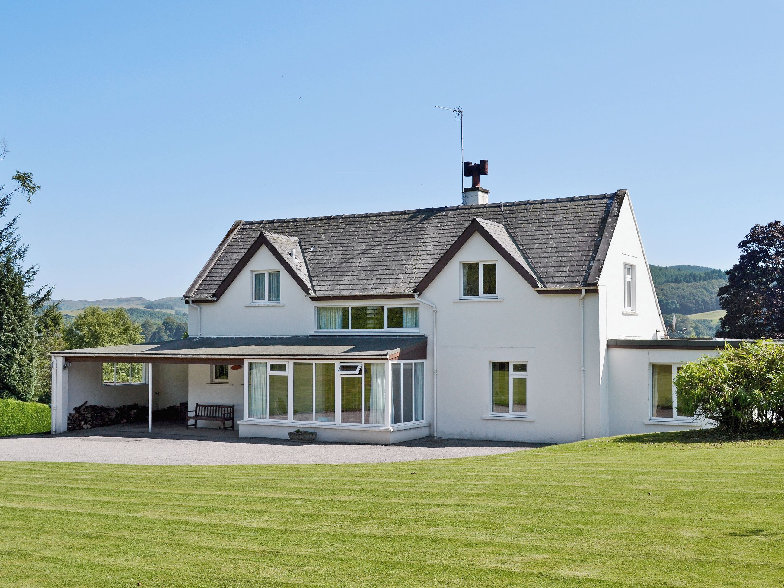 Een tweelaags huis met een groot gazon, een overdekte veranda en een schoorsteen.