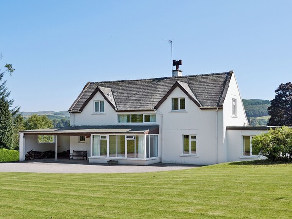 Une maison à deux étages avec une grande pelouse devant, un porche couvert et une cheminée.