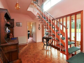Une pièce spacieuse dotée d’un parquet en bois disposé en chevrons, d’un escalier en bois avec des marches recouvertes d’un revêtement vert, et offrant une vue sur l’extérieur grâce à de grandes fenêtres.