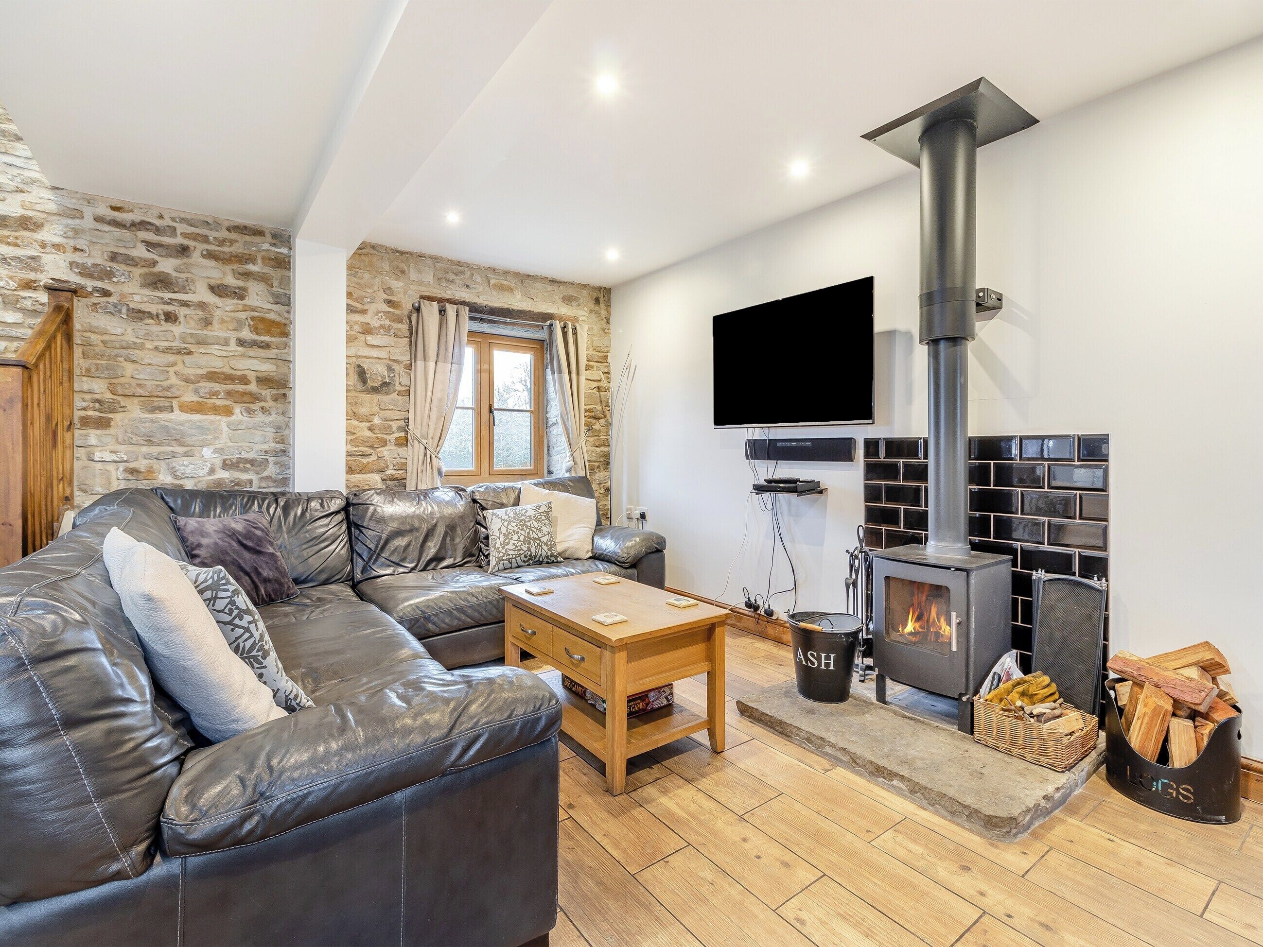 Una sala de estar acogedora con pared de piedra, chimenea, sofá de cuero y televisor.
