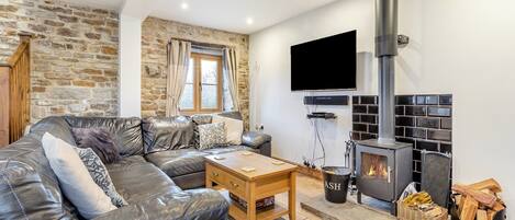 Una sala de estar acogedora con pared de piedra, chimenea, sofá de cuero y televisor.