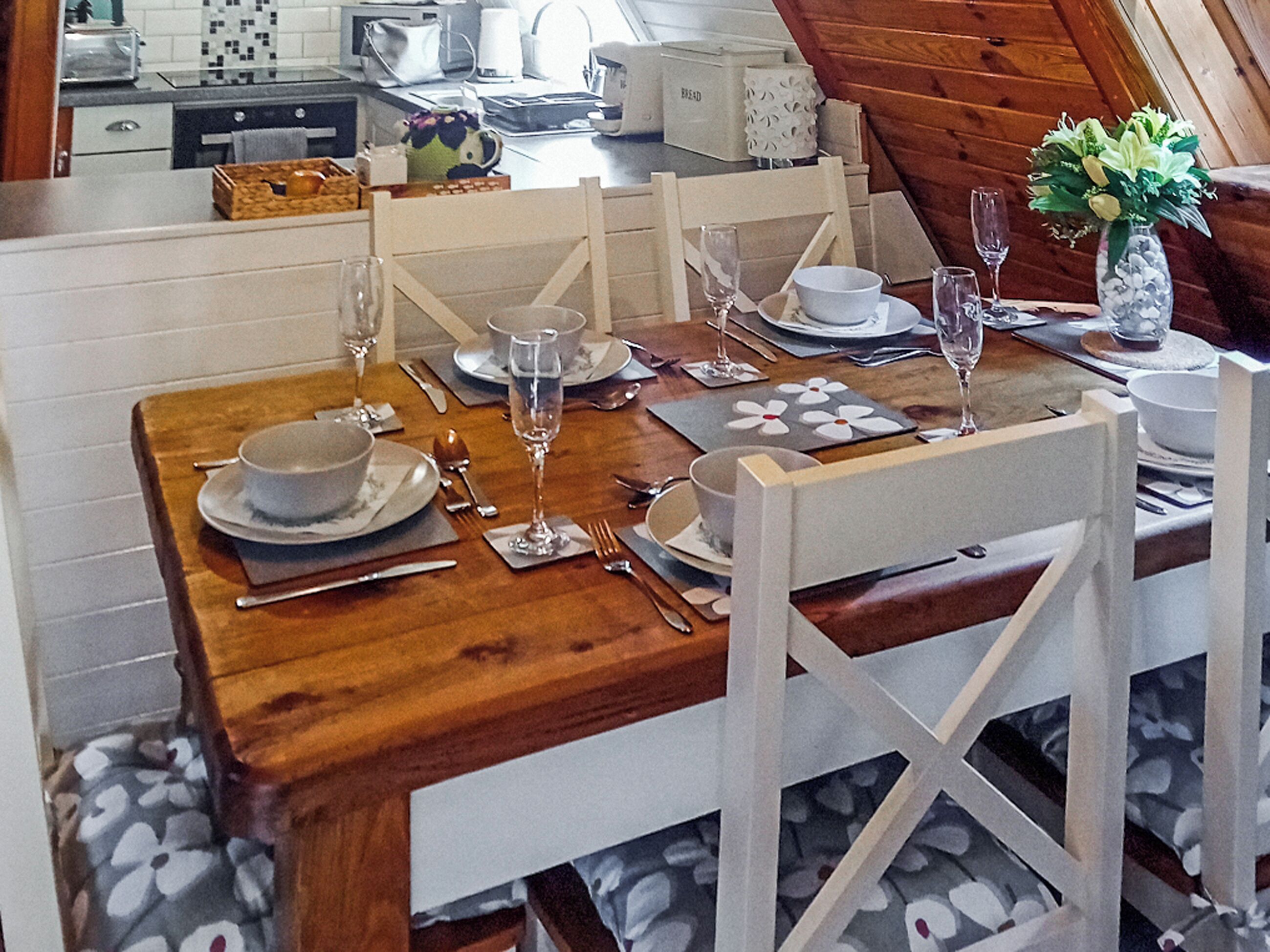 Une table à manger dressée avec des assiettes, des couverts et des verres, entourée de chaises blanches à l’assise recouverte d’un tissu à motifs floraux.