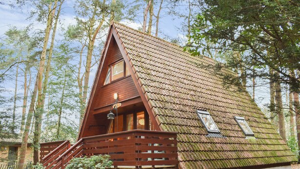 Une cabane en bois avec un toit à forte pente, un escalier en bois et un petit porche.
