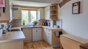 A compact kitchen with wooden cabinets, a dishwasher, a sink, and a small table. - 3 bedroom accommodation in Chickerell, near Weymouth (Chickerell, near Weymouth)