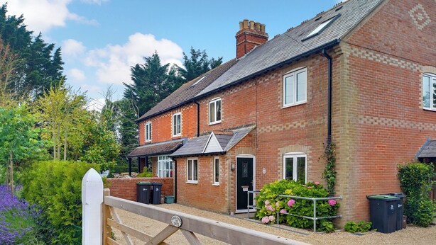 A brick house with a front porch, a gated driveway, and a garden with flowers. - 3 bedroom accommodation in Chickerell, near Weymouth (Chickerell, near Weymouth)