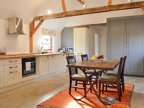 A kitchen with wooden beams, a dining table with chairs, and a fruit bowl.