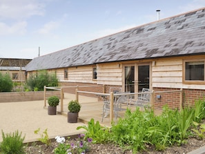 A wooden building with a sloped roof, a fenced outdoor area with potted plants, and a brick wall.