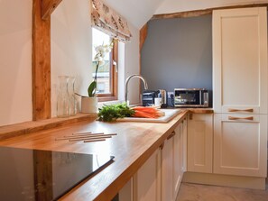 A kitchen with a wooden countertop, a sink, a microwave, and a window with a view.