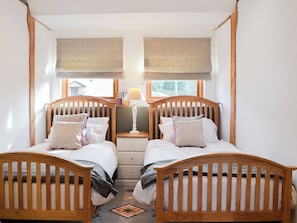 A bedroom with two wooden beds, a nightstand, a lamp, and a window with a view of the outside.