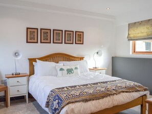 Une chambre à coucher avec un lit en bois, du linge de lit blanc, un plaid à motifs, des tables de chevet avec des lampes et des tableaux encadrés accrochés au mur.