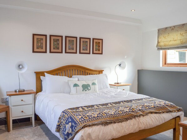 A bedroom with a wooden bed, white bedding, a patterned throw blanket, bedside tables with lamps, and framed pictures on the wall.