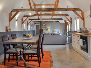 A dining area with a wooden table, chairs, and a fruit bowl. There is a kitchen area with a toaster and a sink.