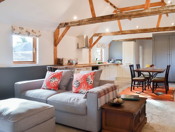 A cozy living room with a sofa, a dining table with chairs, and a kitchen area in the background.