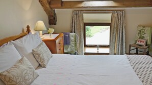 Un dormitorio con una cama grande, una mesita de noche con lámpara, una ventana con cortinas y vistas al exterior.