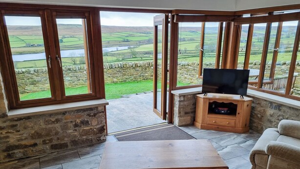 A cozy living room with a stone wall, a wooden table, and a TV on a wooden stand. - 1 bedroom accommodation in Baldersdale, near Barnard Castle (Baldersdale, near Barnard Castle)
