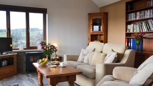 A cozy living room with a sofa, a coffee table with fruits and a lamp, a bookshelf, and a television on a wooden cabinet. - 1 bedroom accommodation in Baldersdale, near Barnard Castle (Baldersdale, near Barnard Castle)