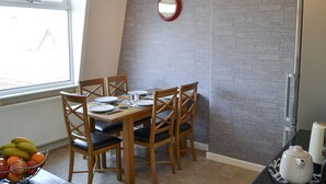 A dining area with a table set for four, wooden chairs, a fruit bowl, and a wall with printed text. - 3 bedroom accommodation in Cromer (Cromer)