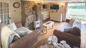 A living room with a stone wall, a television, a white cabinet, and a sofa. - 2 bedroom accommodation in Pyworthy, near Holsworthy (Pyworthy, near Holsworthy)