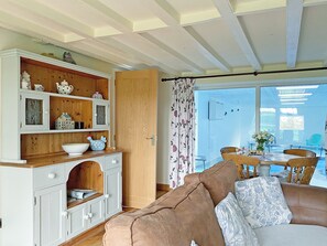 A cozy living room with a sofa, a wooden cabinet with decorative items, and a view of an outdoor dining area. - 2 bedroom accommodation in Pyworthy, near Holsworthy (Pyworthy, near Holsworthy)
