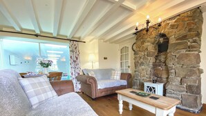 A cozy living room with a stone wall, a wooden coffee table, and a sofa with a plaid throw. - 2 bedroom accommodation in Pyworthy, near Holsworthy (Pyworthy, near Holsworthy)