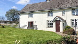 Une maison à deux étages, avec une façade blanche, une porte rouge et une cheminée.