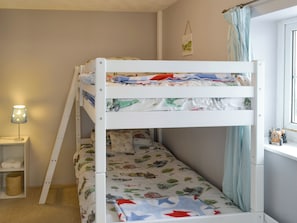 A bunk bed with a lower bunk, a bedside table with a lamp, a small shelf with a basket, and a window with curtains. - 2 bedroom accommodation in Pyworthy, near Holsworthy (Pyworthy, near Holsworthy)
