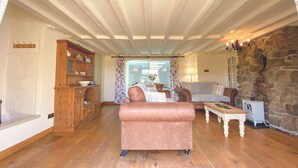 Un salon chaleureux avec un parquet en bois, un canapé rose, un mur en pierre et un buffet en bois contenant de la vaisselle.