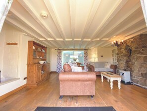 A cozy living room with wooden flooring, a pink sofa, a stone wall, and a wooden cabinet with dishes. - 2 bedroom accommodation in Pyworthy, near Holsworthy (Pyworthy, near Holsworthy)
