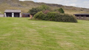 A rural landscape with a grassy field, a small building with a garage, and a hill in the background. - 1 bedroom accommodation in Hapton (Hapton)