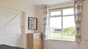 A bedroom with a bed, a dresser, a window with curtains, a radiator, and a door. - 1 bedroom accommodation in Hapton (Hapton)