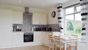 A modern kitchen with white cabinets, a built-in oven, and a dining area with a table and chairs. - 1 bedroom accommodation in Hapton (Hapton)