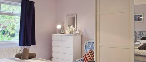 Een slaapkamer met twee bedden, een dressoir, een spiegel en een raam met gordijnen.