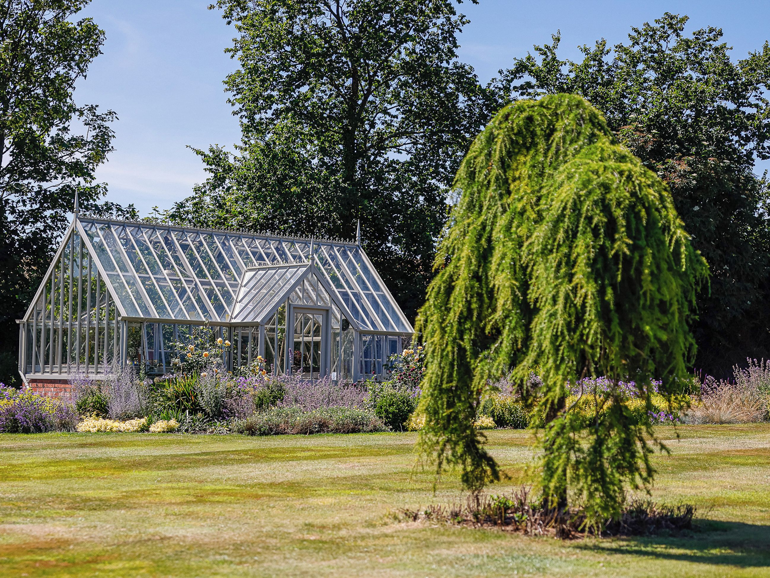 A greenhouse with a glass roof and walls, surrounded by a well-maintained garden with various plants and flowers.