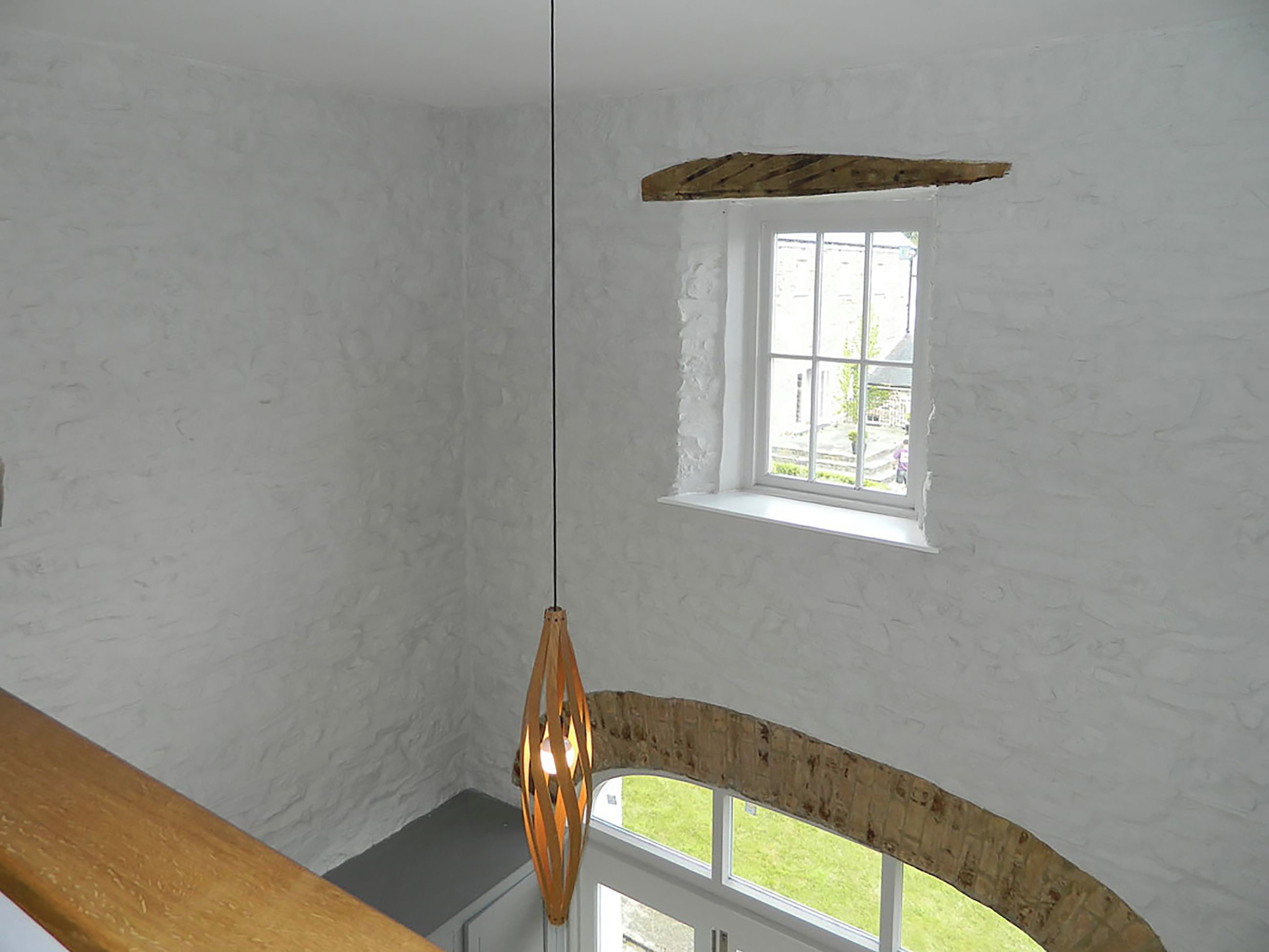 A room with a sloped ceiling, a small window with a view of greenery, and a hanging light fixture.
