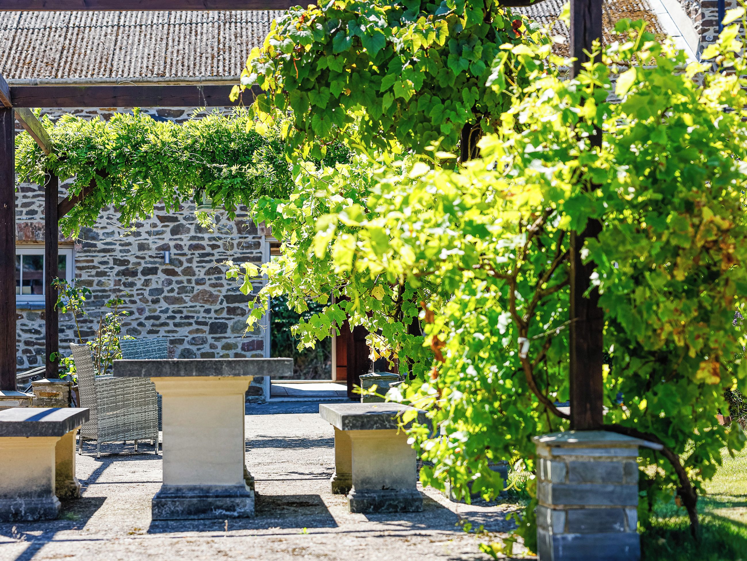 A stone building with a tiled roof, surrounded by greenery and stone benches.